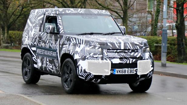 Ein Prototyp des Land Rover Defender mit auffälliger Tarnlackierung fährt auf einer Straße.