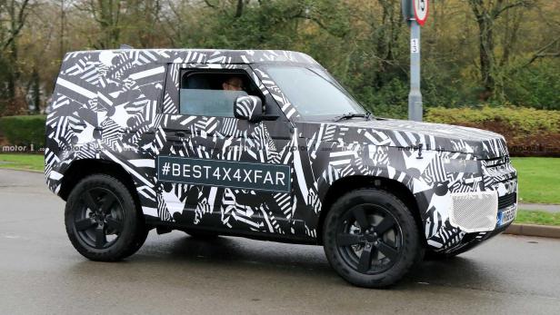 Ein Prototyp des Land Rover Defender mit auffälliger Tarnlackierung fährt auf einer Straße.