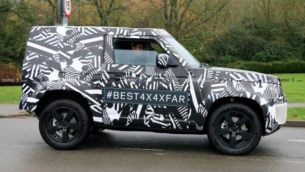 Ein Prototyp des Land Rover Defender mit auffälliger Schwarz-Weiß-Tarnung fährt auf einer Straße.