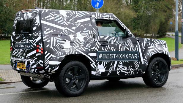 Ein Prototyp des Land Rover Defender mit auffälliger Tarnung fährt auf einer Straße.
