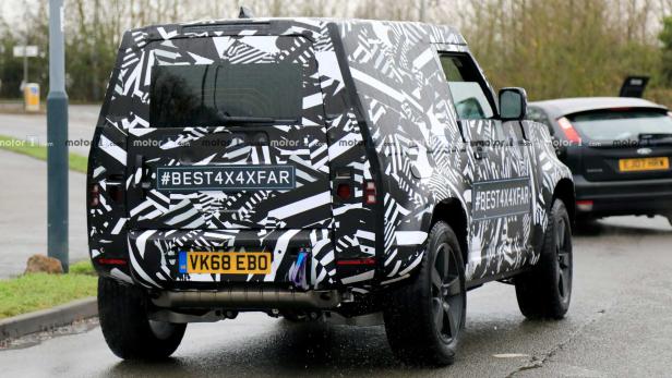 Ein mit einem Muster getarnter Land Rover Defender auf einer Straße.