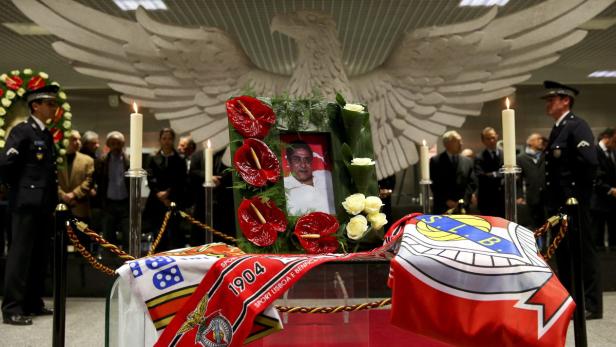 Aufgebahrter Sarg mit Benfica Lissabon-Schals und einem Porträt des Verstorbenen vor einem Adlerdenkmal.