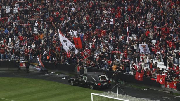 Ein Leichenwagen fährt vor einer Tribüne voller Benfica Lissabon-Fans entlang.