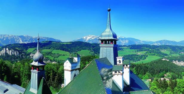 Blick auf die grüne Landschaft und die schneebedeckten Berge von einem Schloss aus.