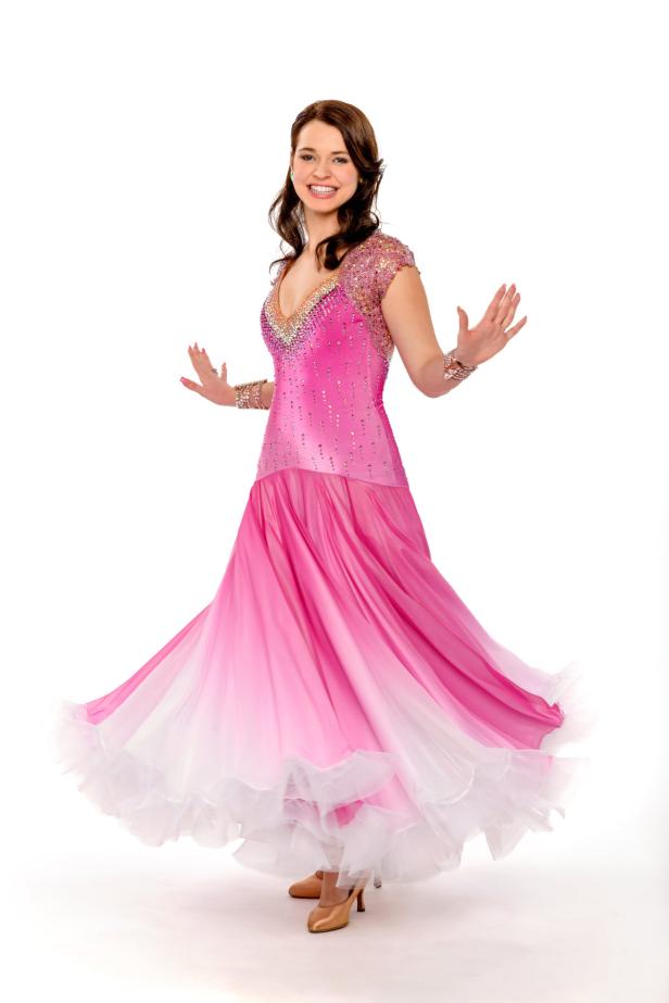 Eine lächelnde Frau in einem rosa Ballkleid mit Strasssteinen und weitem Rock.