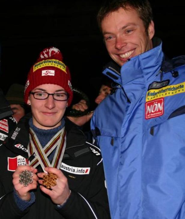 Eine Skispringerin mit Medaillen und ein Mann in Sportkleidung lächeln in die Kamera.