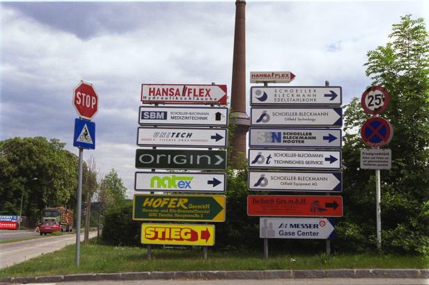 Ein Straßenschild mit Hinweisen zu verschiedenen Firmen, darunter Hansa Flex und Schoeller-Bleckmann.