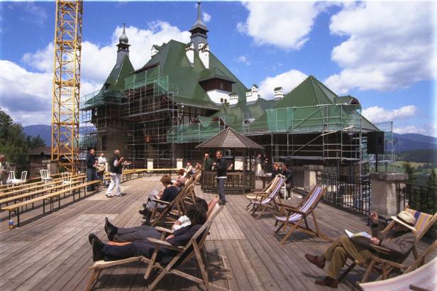 Menschen entspannen sich auf Liegestühlen vor einem Schloss, das von einem Gerüst umgeben ist.