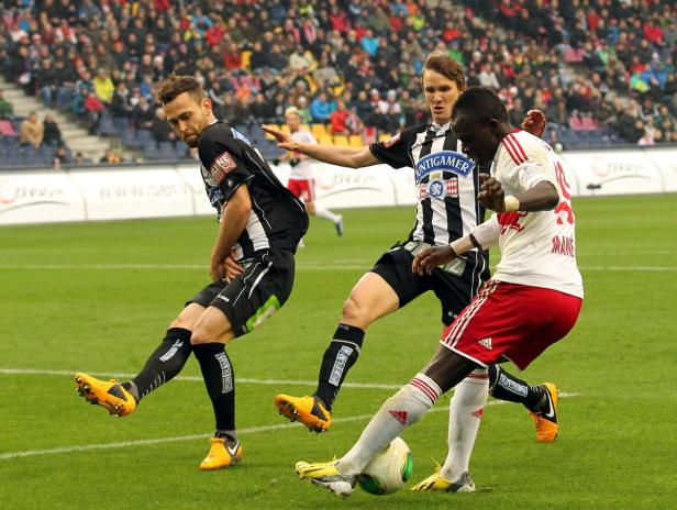 Drei Fußballspieler kämpfen um den Ball auf dem Spielfeld.