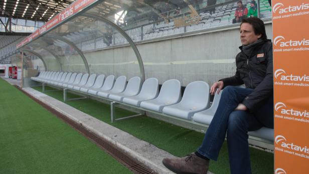 Ein Mann sitzt in der Trainerbank eines Fußballstadions.