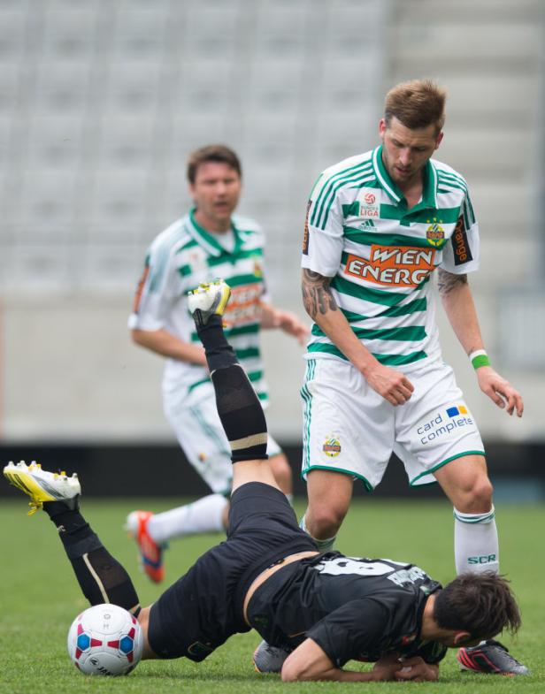 Ein Fußballspieler liegt am Boden, während ein anderer Spieler zusieht.
