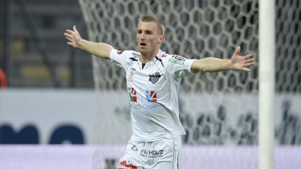Ein Fußballspieler jubelt mit ausgestreckten Armen vor einem Tornetz.