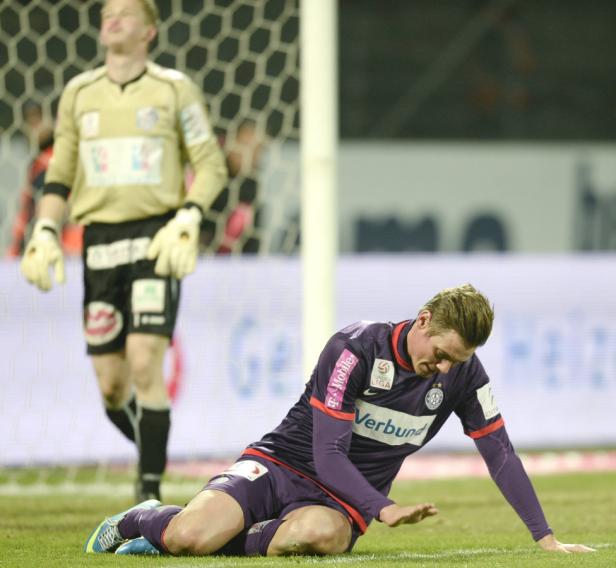 Ein Fußballspieler kniet enttäuscht auf dem Rasen, im Hintergrund ein Torwart.