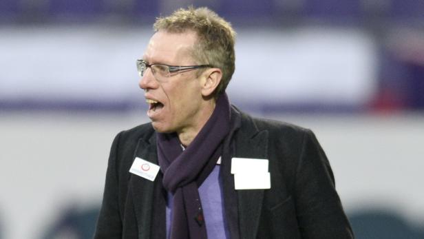 Ein Mann mit Brille und Schal gestikuliert auf einem Fußballfeld.