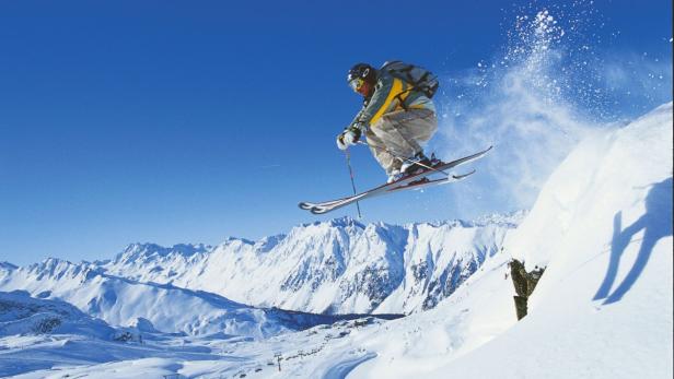 Ein Skifahrer springt vor einer verschneiten Berglandschaft.