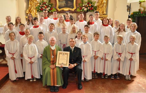 Eine Gruppe von Kindern in weißen Gewändern steht mit einem Priester und einem Mann in einer Kirche.