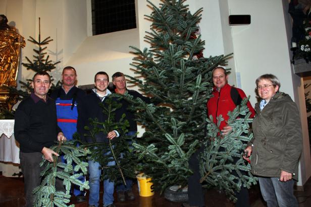 Eine Gruppe von Menschen schmückt einen Weihnachtsbaum in einer Kirche.