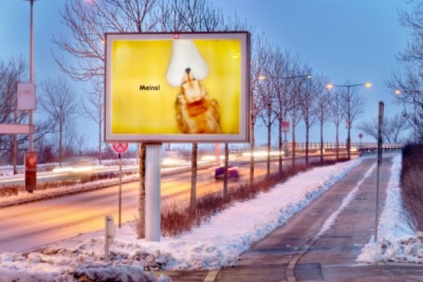 Eine Werbetafel am Straßenrand zeigt ein Küken mit der Aufschrift „Meins!“.