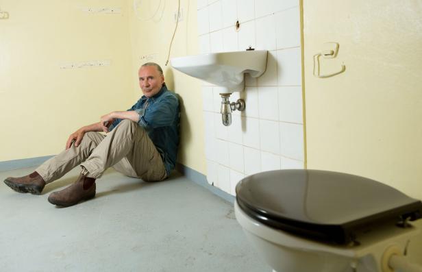 Ein Mann sitzt in einem heruntergekommenen Badezimmer auf dem Boden.