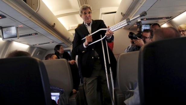John Kerry steht mit Krücken in einem Flugzeug und wird fotografiert.