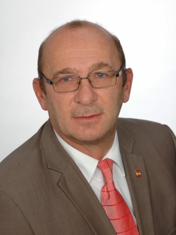 Ein Mann mit Brille, Anzug und Krawatte blickt in die Kamera.