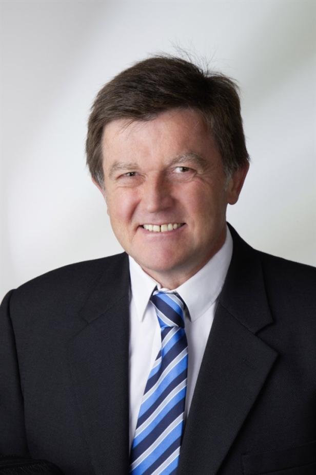 Ein lächelnder Mann im Anzug mit blau-gestreifter Krawatte.
