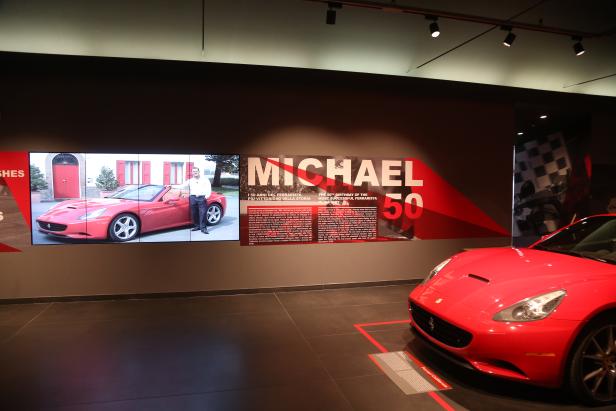 Ein roter Ferrari California steht in einem Ausstellungsraum neben Informationstafeln über Michael Schumacher.
