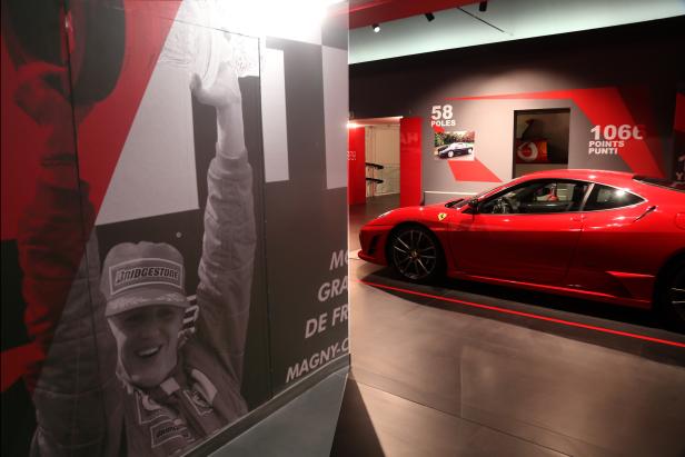 Ein roter Ferrari steht in einem Ausstellungsraum neben einem Porträt von Michael Schumacher.