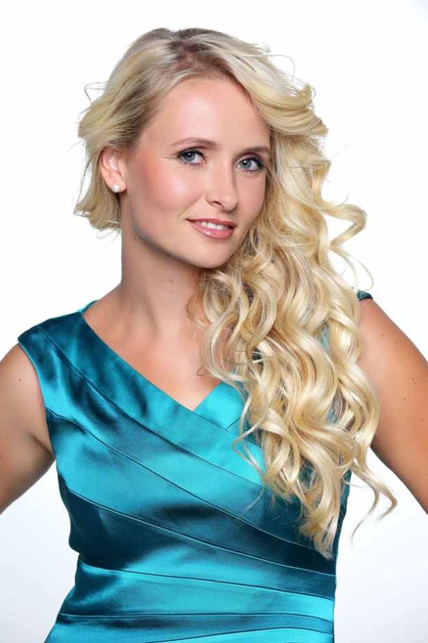 Eine blonde Frau in einem türkisfarbenen Kleid lächelt in die Kamera.