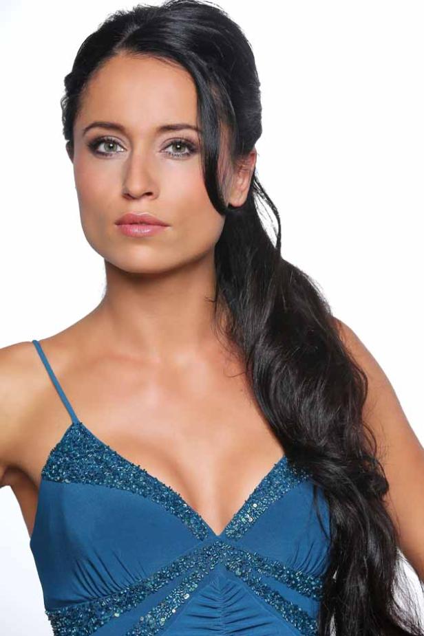 Eine Frau mit dunklen Haaren und einem blauen, paillettenbesetzten Kleid blickt in die Kamera.