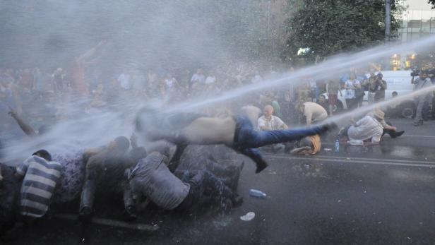 Ein Wasserwerfer trifft eine Gruppe von Demonstranten auf der Straße.