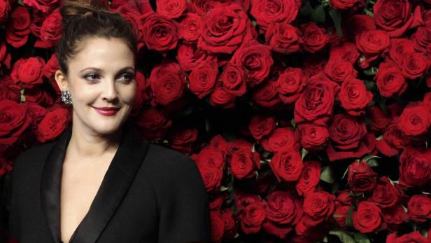 Drew Barrymore posiert vor einer Wand aus roten Rosen.