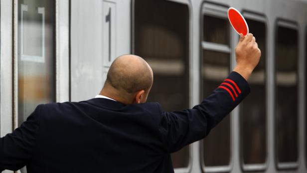 An employee of German rail operator Deutsche Bahn Ein Zugbegleiter mit roter Kelle gibt ein Signal vor einem Zug.