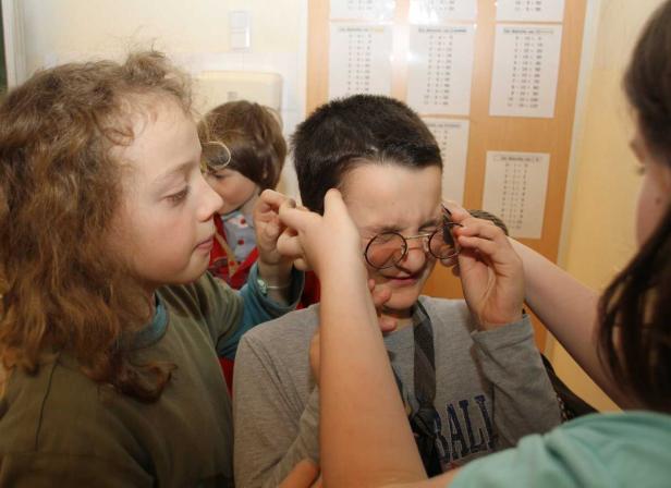 Mehrere Kinder helfen einem Jungen, seine Brille anzupassen.