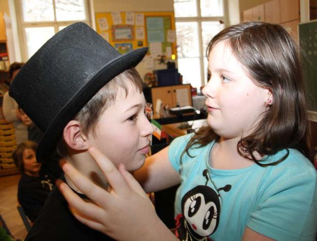 Ein Mädchen berührt das Gesicht eines Jungen mit Zylinder.