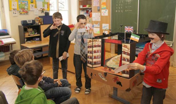 Schüler präsentieren ein Projekt mit Flaggen und einem Modellgebäude im Klassenzimmer.