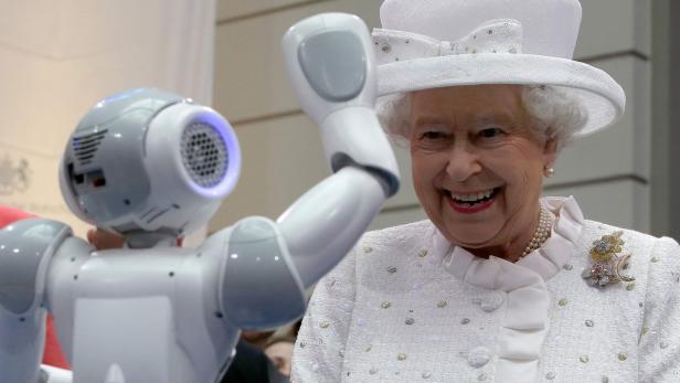 Königin Elisabeth II. lächelt neben einem Roboter, der seinen Arm hebt.