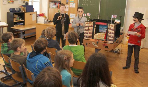 Schüler präsentieren ein Projekt mit Flaggen und einem Modell vor einer Klasse.
