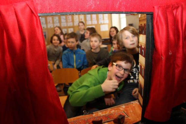 Eine Gruppe von Schulkindern blickt durch einen roten Theatervorhang.