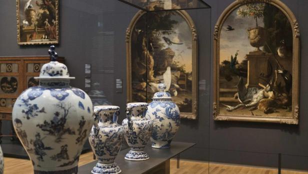 In einem Museum stehen blau-weiße Porzellanvasen vor Gemälden.
