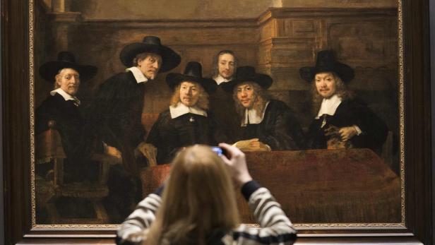 Eine Frau fotografiert Rembrandts „Die Vorsteher der Tuchmacherzunft“ in einem Museum.