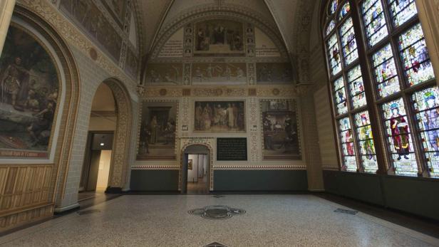 Ein großer Saal mit Wandmalereien und einem Buntglasfenster.
