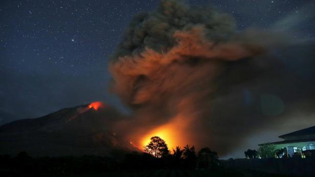 Ein Vulkan bricht nachts aus und speit Rauch und Lava unter einem Sternenhimmel.