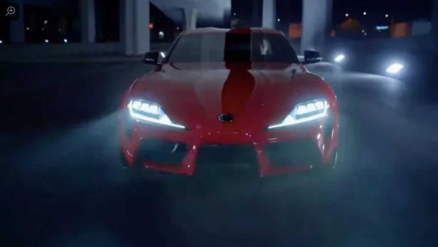 Ein roter Toyota Supra mit eingeschalteten Scheinwerfern in der Nacht.