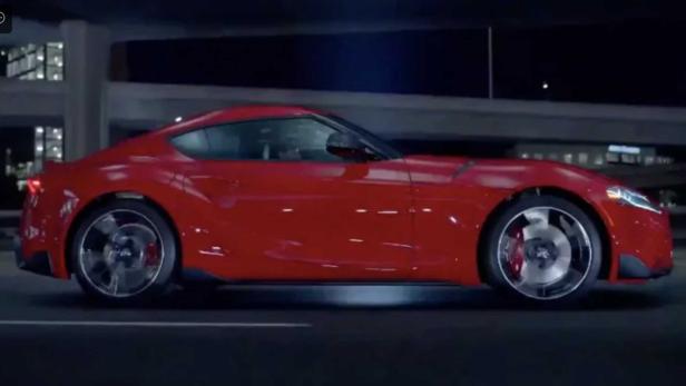 Ein roter Toyota Supra fährt auf einer dunklen Straße.