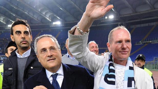 Mehrere Männer stehen auf einem Fußballfeld, einer winkt mit der Hand.