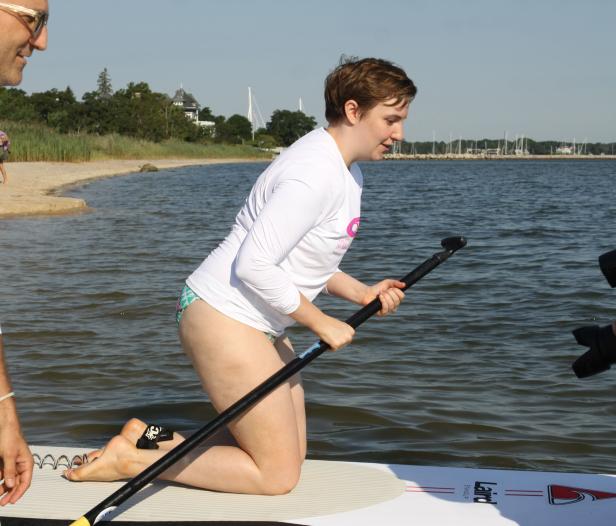 Eine Frau kniet auf einem Paddleboard und hält ein Paddel.