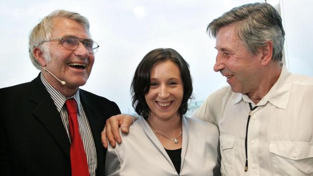 Drei lächelnde Personen stehen nebeneinander vor einem hellen Hintergrund.