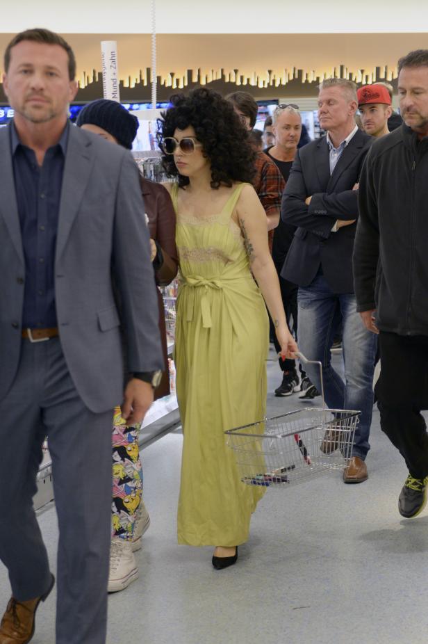 Eine Frau mit Afro-Frisur und Sonnenbrille schiebt einen Einkaufswagen durch einen Laden.