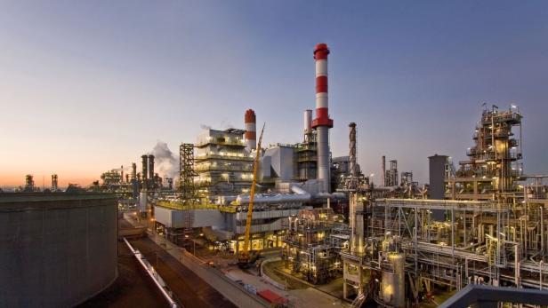 Eine große Industrieanlage mit vielen Rohren und Schornsteinen bei Dämmerung.
